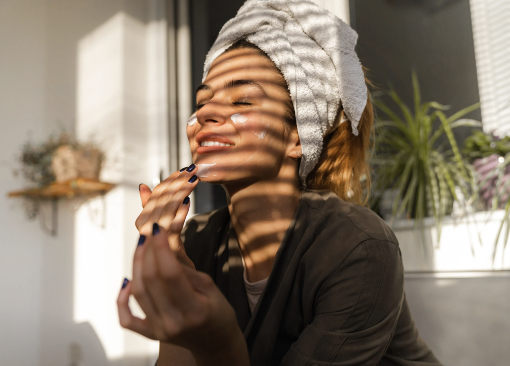 A mother applying face cream with a towel wrapped around her head, depicting that she is taking time to take care of herself.
