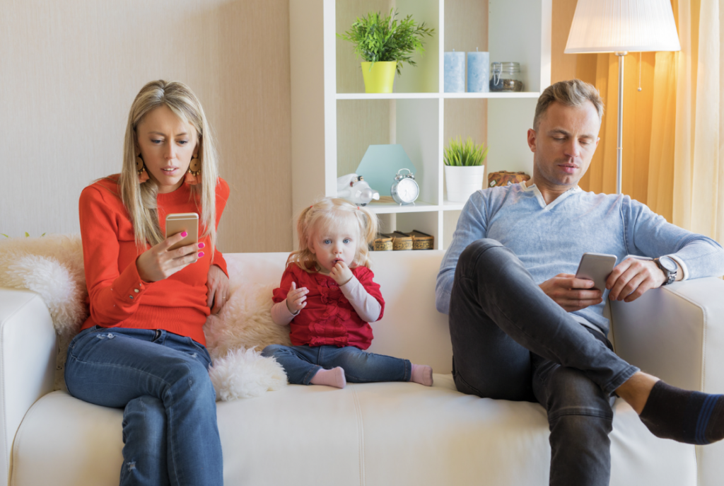 Two parents on their phone in front of their child; depicting the importance of disconnecting from our phones, for the wellbeing our our child(ren).